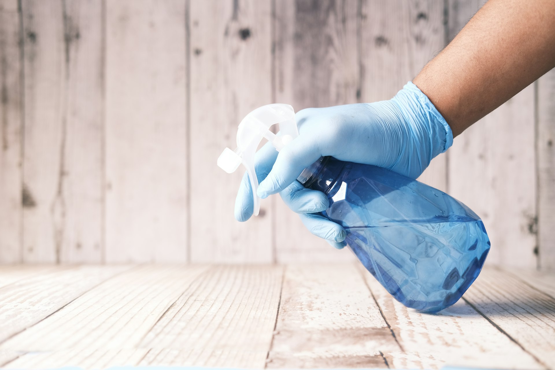 Gloved hand holding a cleaning chemical spray bottle